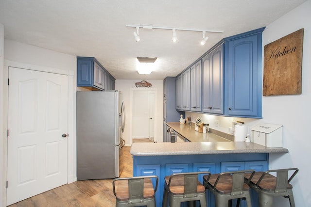 kitchen featuring blue cabinets, stainless steel fridge, kitchen peninsula, and light hardwood / wood-style flooring