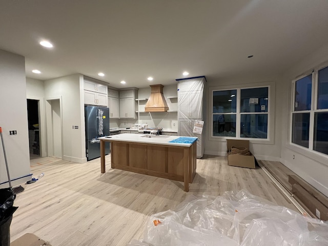 kitchen with a kitchen bar, custom exhaust hood, a center island, light hardwood / wood-style floors, and black fridge