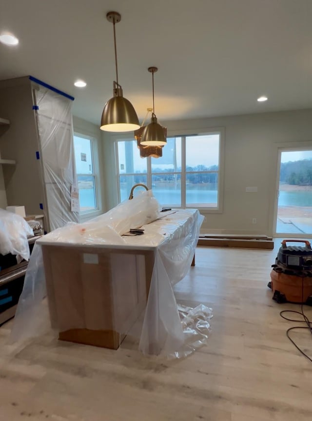 kitchen with a water view, light stone counters, hanging light fixtures, light hardwood / wood-style floors, and a baseboard heating unit