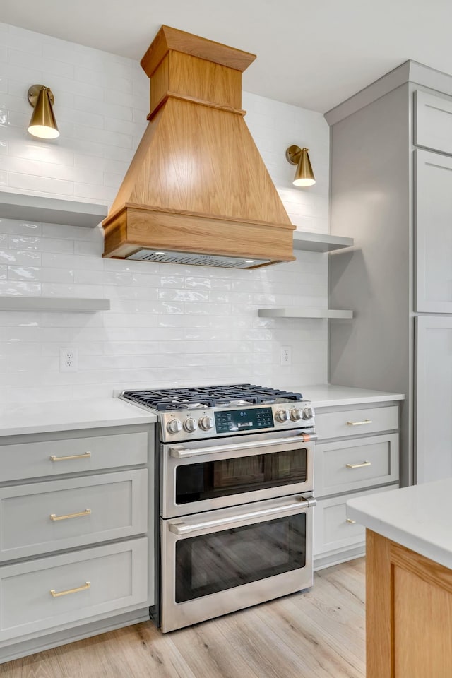 kitchen featuring custom exhaust hood, light countertops, double oven range, open shelves, and backsplash