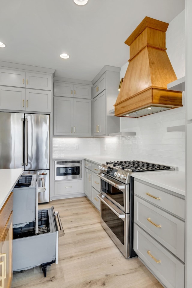 kitchen featuring light wood finished floors, light countertops, appliances with stainless steel finishes, tasteful backsplash, and custom range hood