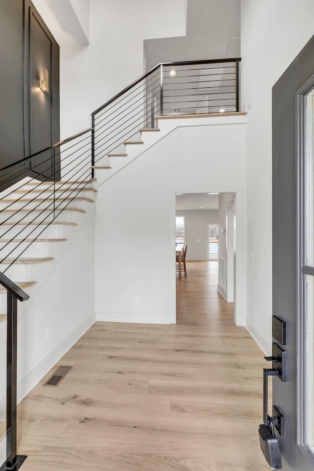 staircase featuring a towering ceiling, wood finished floors, visible vents, and baseboards