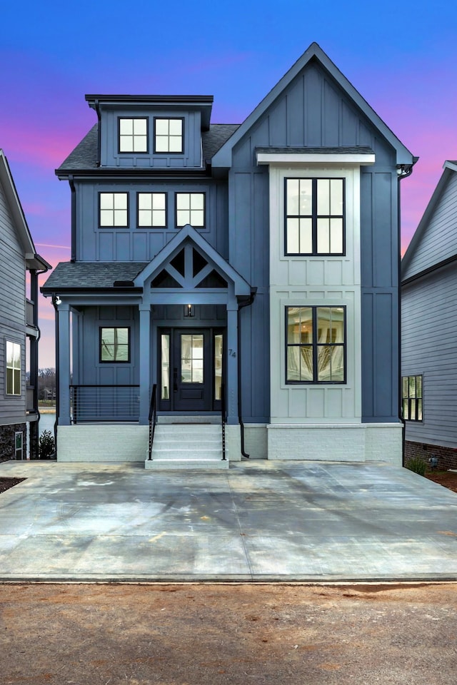 modern inspired farmhouse featuring board and batten siding, covered porch, and roof with shingles