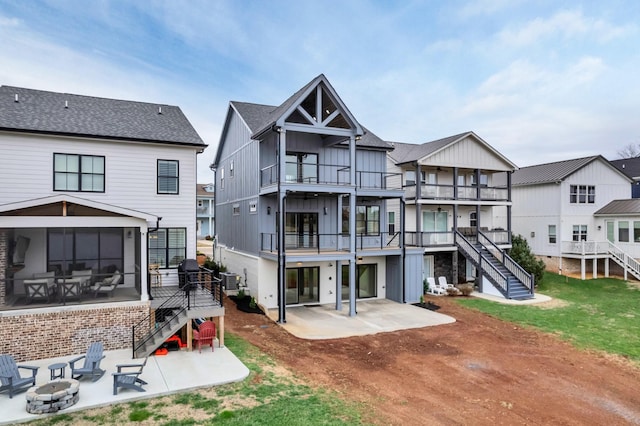 back of property with a fire pit, a patio, a balcony, a sunroom, and stairs