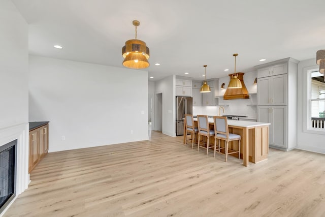 kitchen with a glass covered fireplace, light wood-style flooring, high quality fridge, a breakfast bar, and recessed lighting