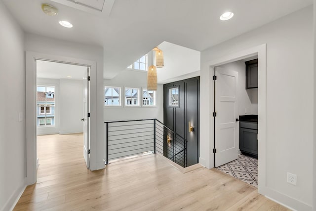 hallway with an upstairs landing, light wood-style flooring, baseboards, and recessed lighting