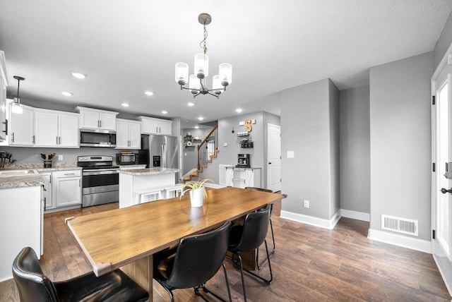 dining space with dark wood-type flooring, an inviting chandelier, and sink