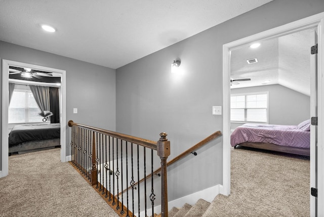 corridor featuring vaulted ceiling, light colored carpet, and a textured ceiling