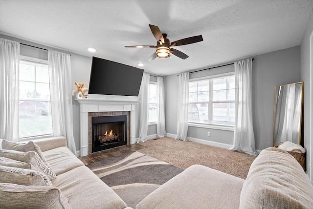 living room with a tiled fireplace, a healthy amount of sunlight, a textured ceiling, and dark carpet