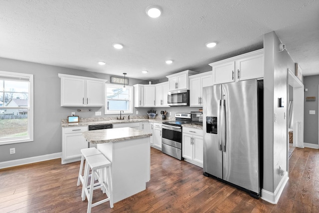 kitchen featuring white cabinetry, stainless steel appliances, decorative light fixtures, and a kitchen island