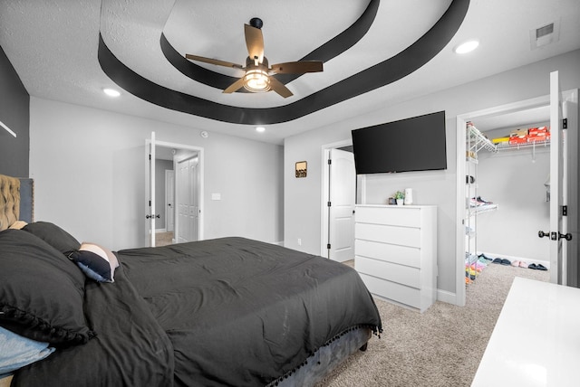 carpeted bedroom with a raised ceiling, a spacious closet, ceiling fan, and a closet