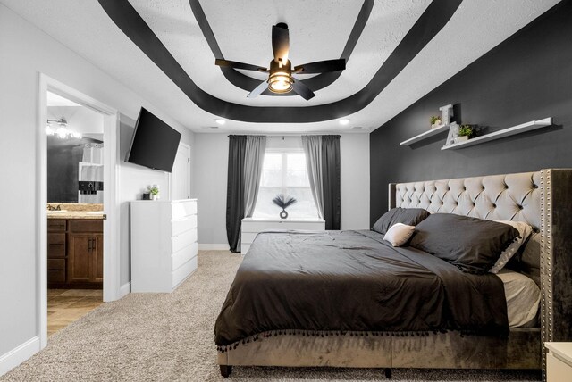 bedroom with ensuite bathroom, light colored carpet, ceiling fan, a tray ceiling, and a textured ceiling