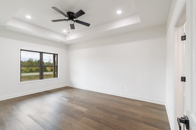 empty room with ceiling fan, dark hardwood / wood-style flooring, and a raised ceiling