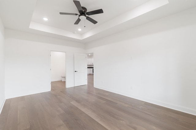 empty room with ceiling fan, light wood-type flooring, and a tray ceiling