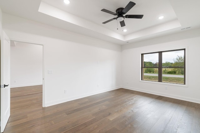 empty room with dark hardwood / wood-style floors, ceiling fan, and a tray ceiling