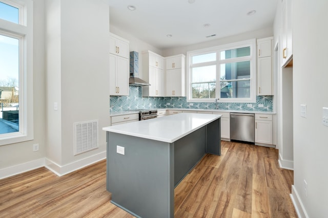 kitchen featuring white cabinetry, appliances with stainless steel finishes, a center island, and wall chimney exhaust hood