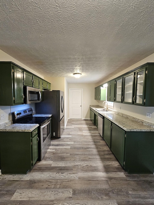 kitchen featuring appliances with stainless steel finishes, hardwood / wood-style flooring, a textured ceiling, green cabinets, and sink