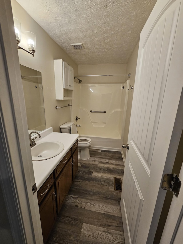 full bathroom featuring shower / washtub combination, toilet, wood-type flooring, a textured ceiling, and vanity