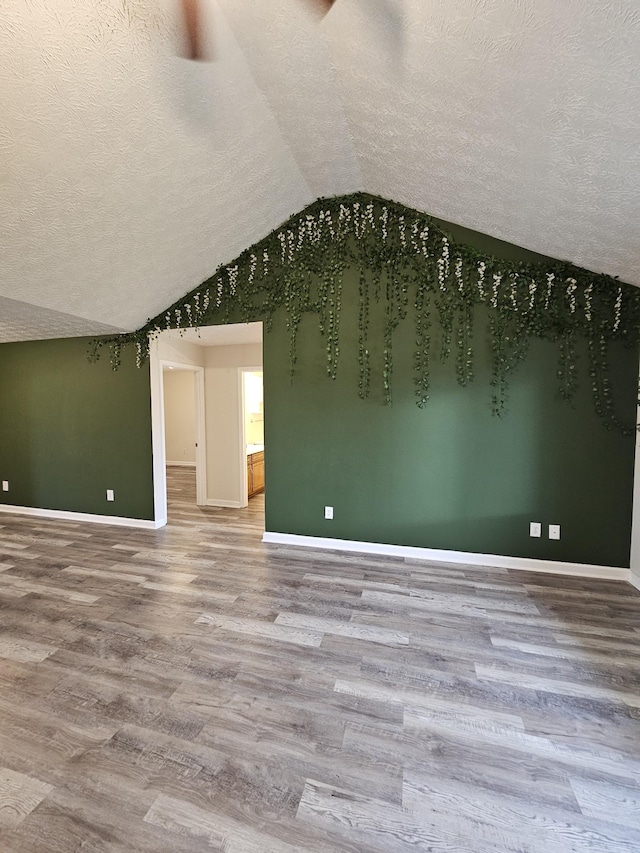 unfurnished room featuring hardwood / wood-style floors, lofted ceiling, and a textured ceiling