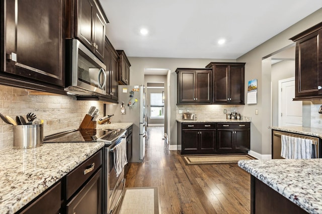 kitchen featuring dark brown cabinetry, stainless steel appliances, baseboards, decorative backsplash, and dark wood finished floors