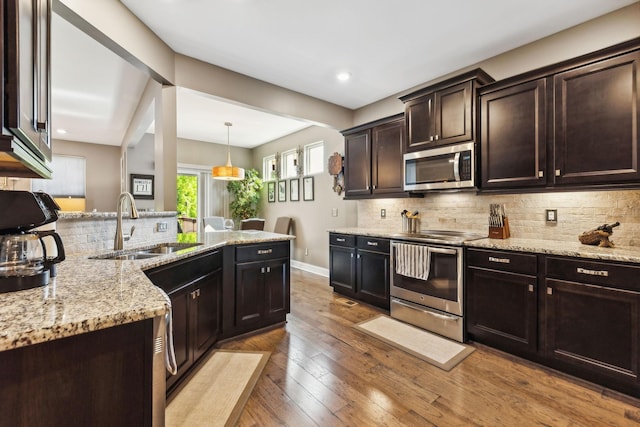 kitchen with light wood-style flooring, dark brown cabinetry, stainless steel appliances, a sink, and hanging light fixtures