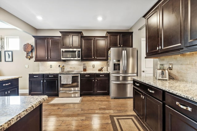 kitchen with stainless steel appliances, tasteful backsplash, dark brown cabinets, and light hardwood / wood-style flooring