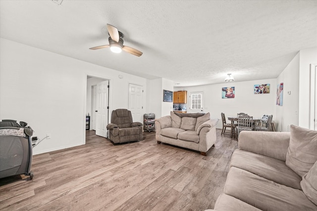 living room featuring ceiling fan, light hardwood / wood-style flooring, and a textured ceiling