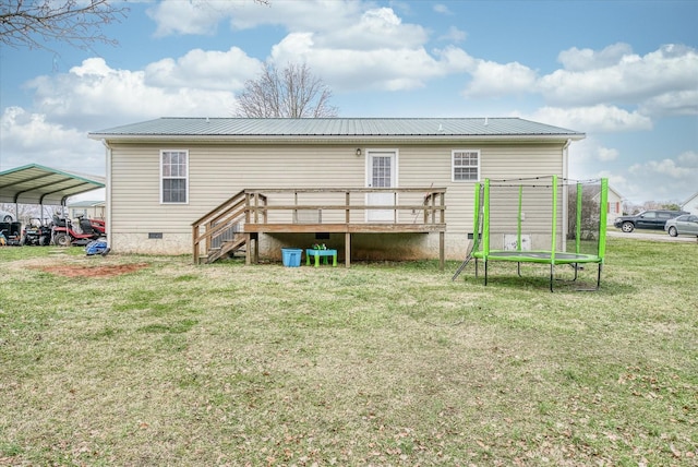 back of house featuring a carport, a deck, a trampoline, and a lawn