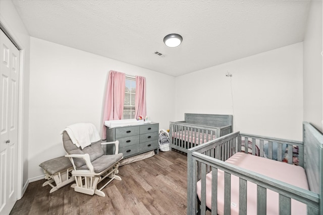 bedroom featuring hardwood / wood-style floors, a crib, a closet, and a textured ceiling