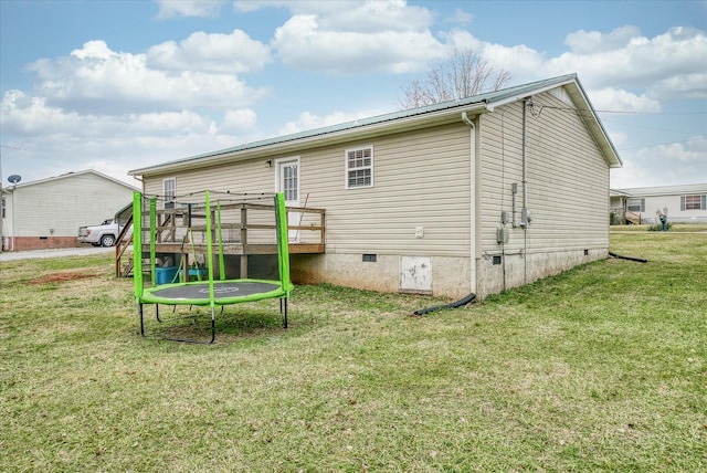 rear view of property with a wooden deck, a trampoline, and a lawn