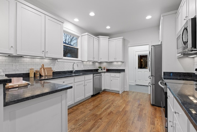 kitchen with white cabinetry, appliances with stainless steel finishes, sink, and dark stone counters