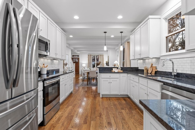 kitchen with appliances with stainless steel finishes, pendant lighting, sink, dark stone countertops, and white cabinets