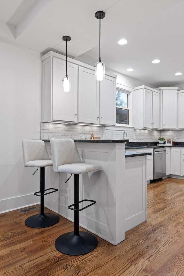 kitchen with dark wood-type flooring, a breakfast bar area, stainless steel dishwasher, pendant lighting, and white cabinets