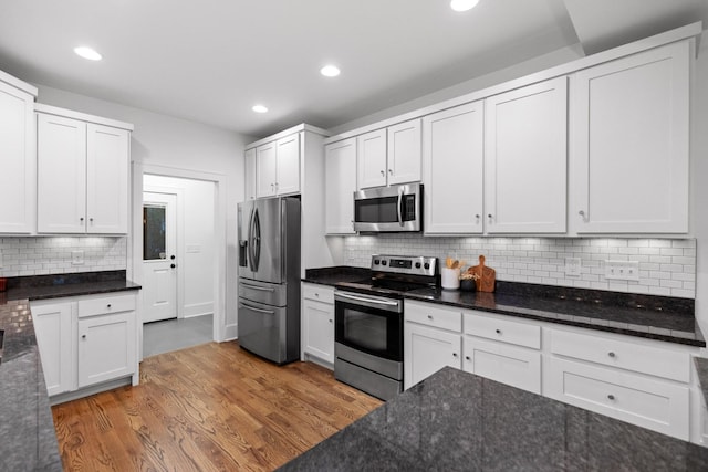 kitchen with white cabinetry, wood-type flooring, decorative backsplash, dark stone counters, and stainless steel appliances