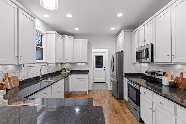 kitchen with sink, white cabinetry, stainless steel appliances, light hardwood / wood-style floors, and dark stone counters