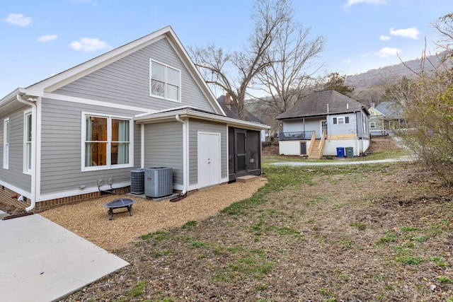 view of side of home with a sunroom, central AC unit, a mountain view, and a fire pit