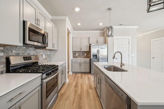 kitchen featuring appliances with stainless steel finishes, decorative light fixtures, an island with sink, sink, and gray cabinetry