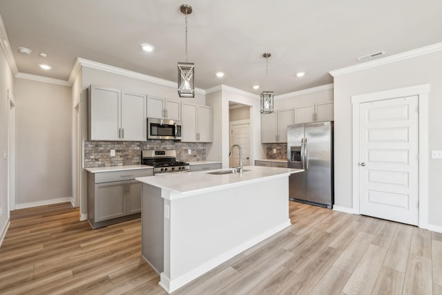 kitchen featuring appliances with stainless steel finishes, decorative light fixtures, an island with sink, sink, and gray cabinetry