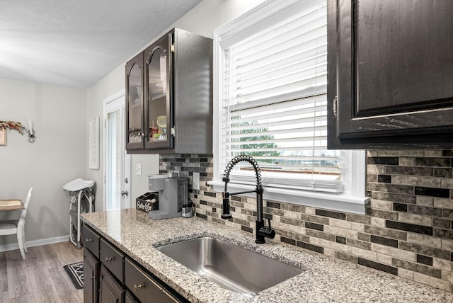 kitchen featuring sink, backsplash, light hardwood / wood-style flooring, and light stone countertops