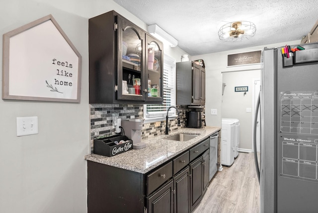 kitchen with sink, light hardwood / wood-style flooring, appliances with stainless steel finishes, backsplash, and washing machine and clothes dryer