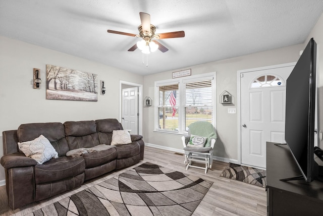 living room with ceiling fan, a textured ceiling, and light wood-type flooring