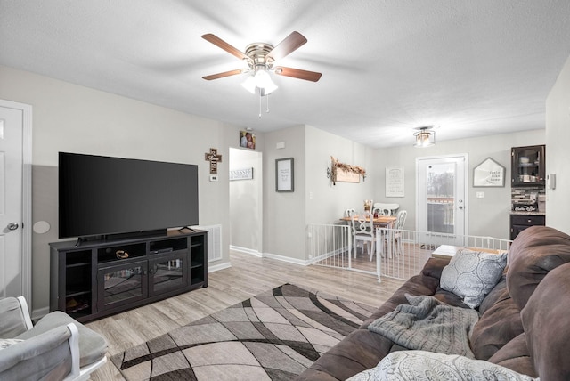 living room with ceiling fan, a textured ceiling, and light wood-type flooring