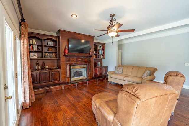 living room featuring a premium fireplace, dark wood-type flooring, ceiling fan, and crown molding