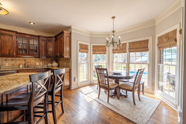 dining space with ornamental molding, sink, a notable chandelier, and light wood-type flooring