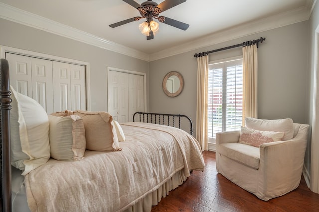 bedroom with crown molding, dark hardwood / wood-style floors, two closets, and ceiling fan