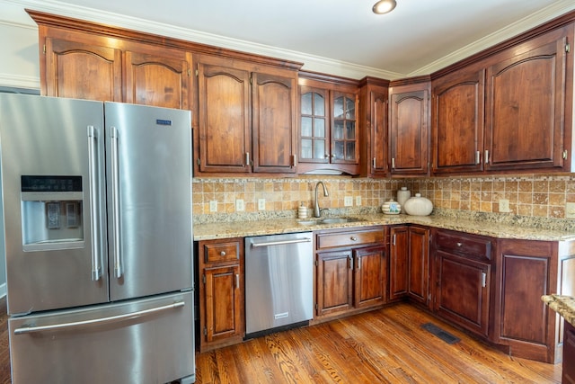 kitchen featuring dark wood-type flooring, sink, light stone counters, stainless steel appliances, and backsplash