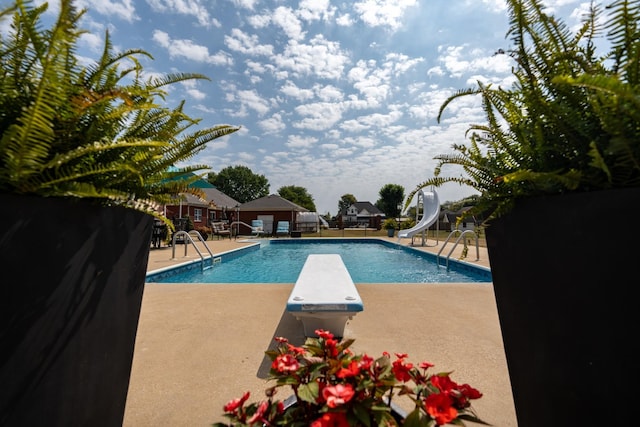 view of pool featuring a water slide, a diving board, and a patio