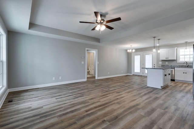 unfurnished living room featuring dark wood-type flooring, a raised ceiling, and ceiling fan with notable chandelier