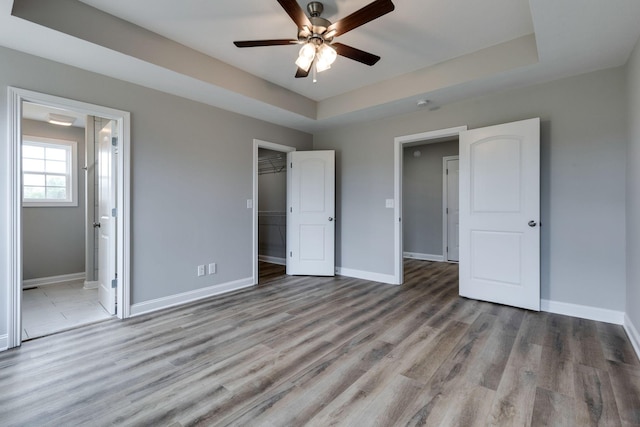 unfurnished bedroom featuring connected bathroom, a spacious closet, light hardwood / wood-style flooring, and a raised ceiling