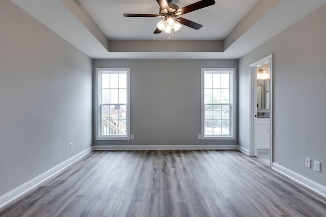 spare room featuring wood finished floors, a raised ceiling, and baseboards